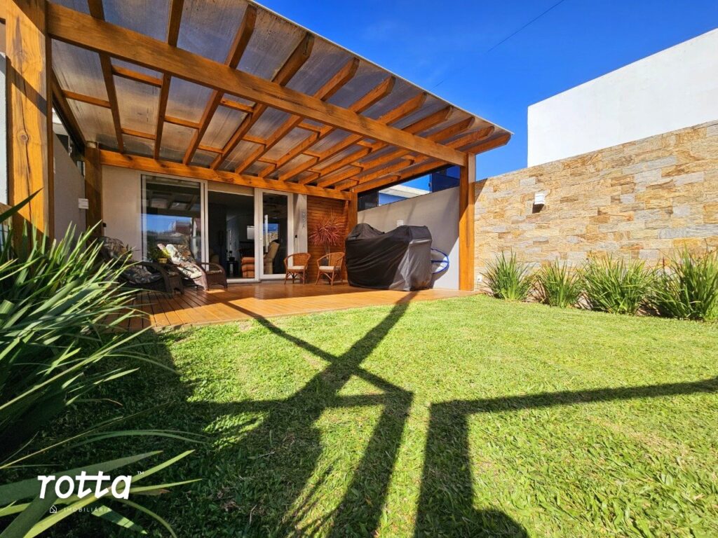 Área externa com pergolado de madeira, móveis de descanso e gramado bem cuidado.
