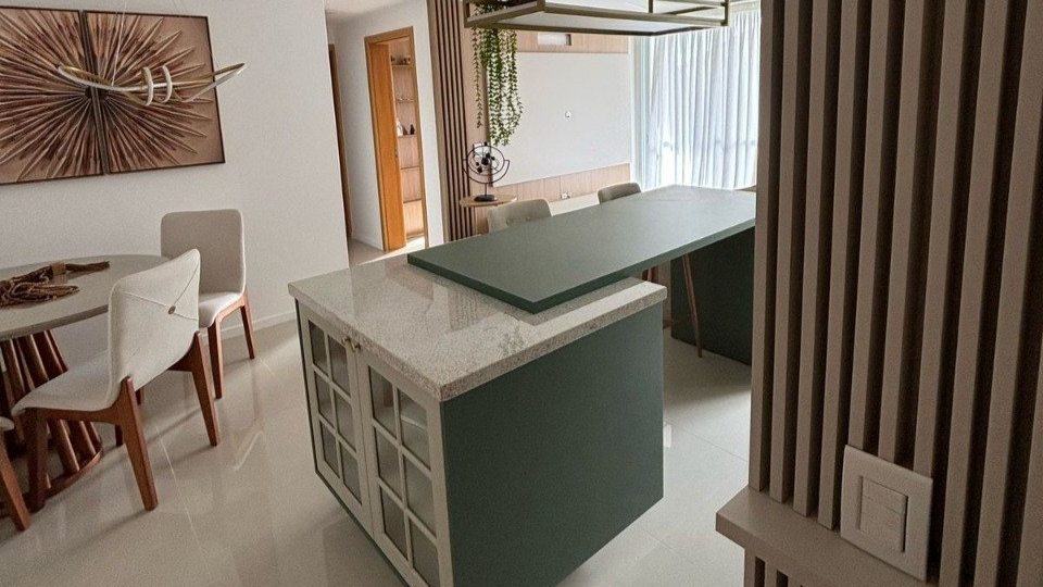 Cozinha moderna com ilha central verde e bancada estendida próxima à sala de jantar.