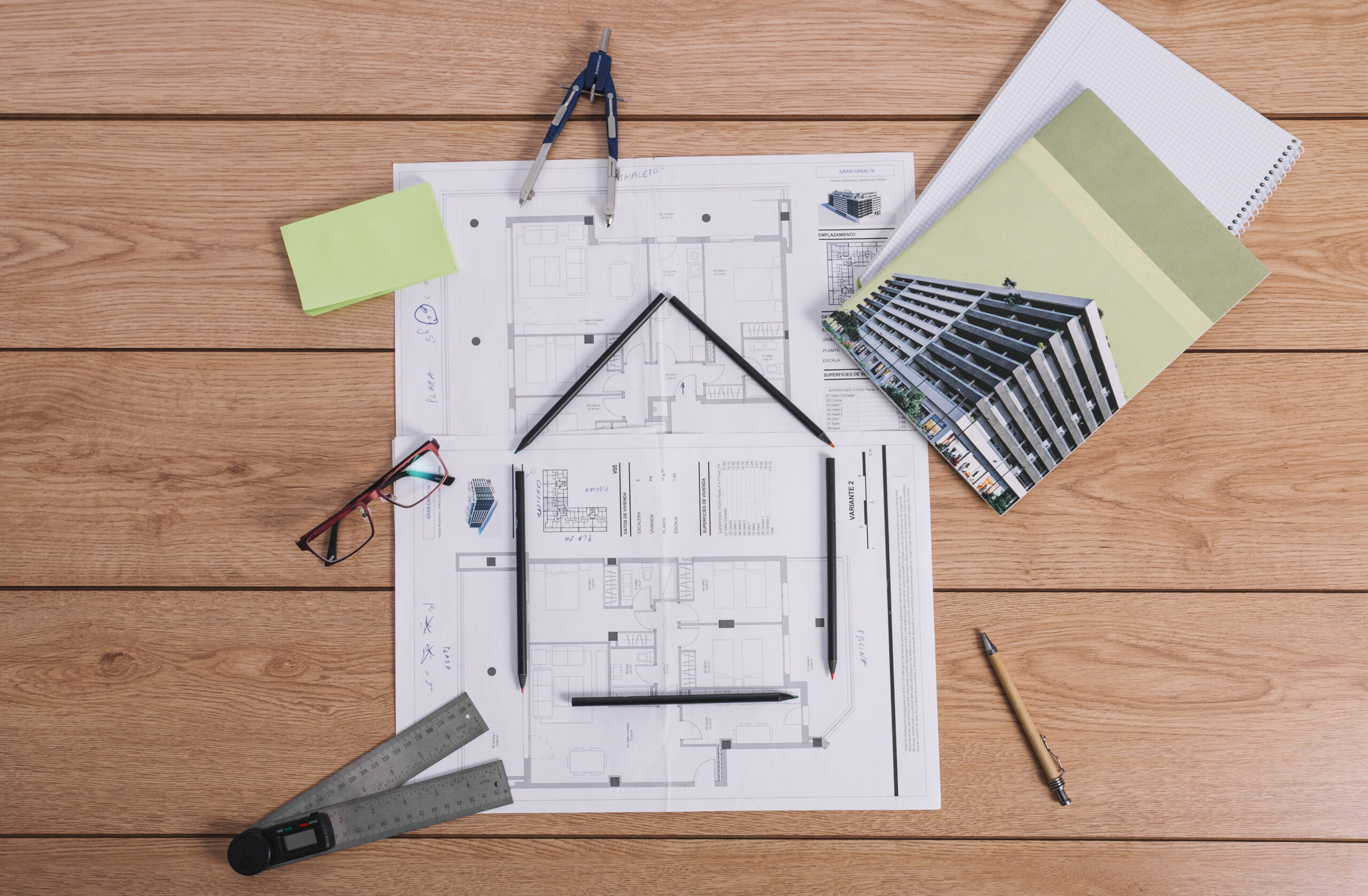 Plantas, régua, lápis e pranchetas sobre uma mesa com plantas arquitetônicas, representando planejamento ou projeto de construção.