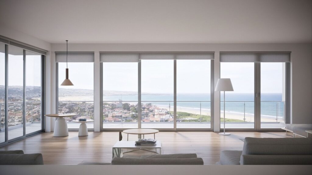 Sala ampla com janelas de vidro e vista panorâmica para o mar e cidade ao fundo.