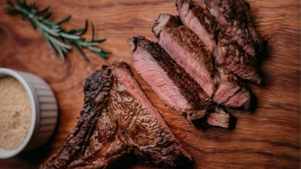 Tábua de madeira rústica servindo um corte de carne nobre fatiada e suculenta ao ponto, decorada com alecrim e acompanhada de farofa, opção gastronômica de churrascarias e restaurantes no Cassino.