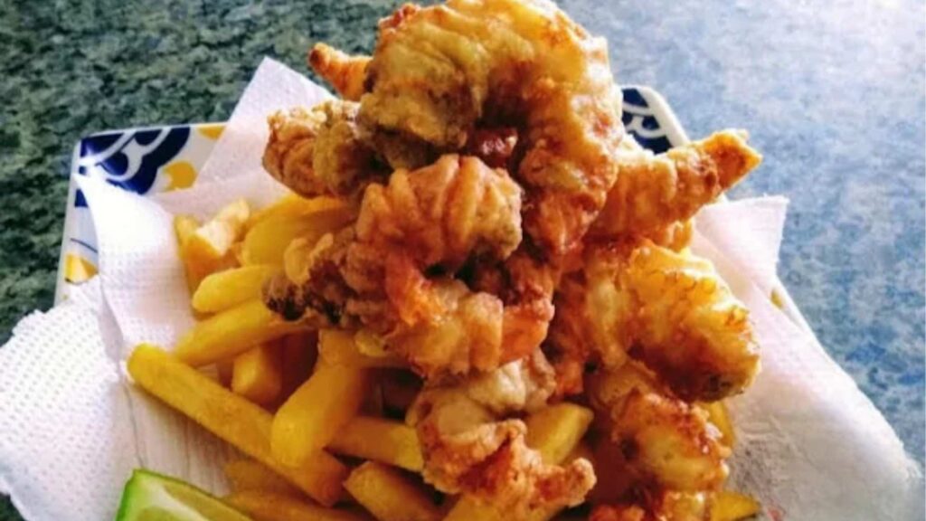 Porção generosa de camarões à milanesa fritos servidos sobre batatas fritas crocantes, acompanhados de um pedaço de limão em um prato, comida típica de restaurantes de frutos do mar no Cassino.