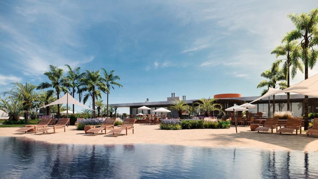 Área de lazer externa com piscina de borda infinita, deck de areia com espreguiçadeiras de madeira, guarda-sóis e lounge ao ar livre cercado por paisagismo tropical.