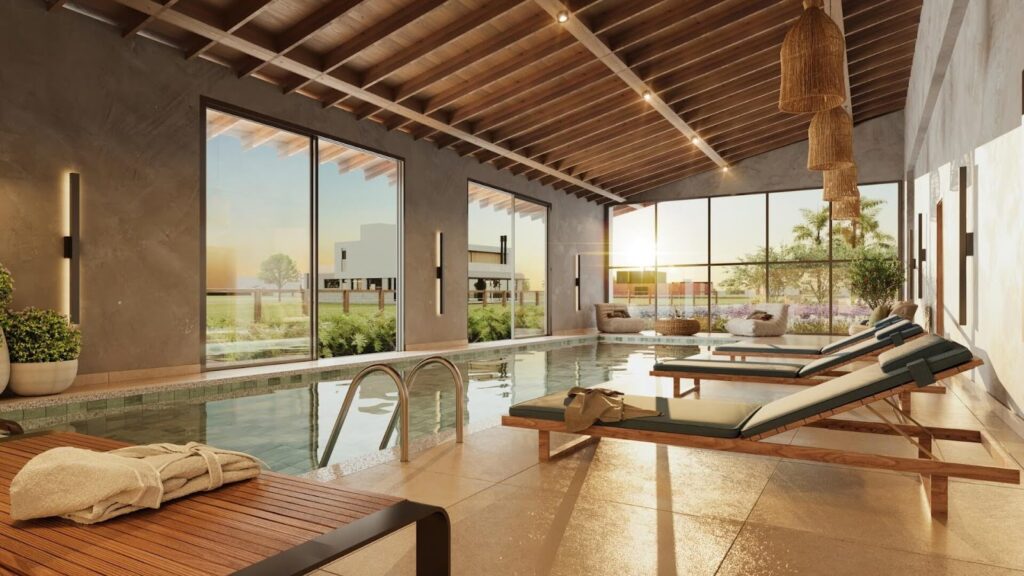 Piscina interna aquecida com teto amadeirado, grandes janelas de vidro com vista para o jardim, espreguiçadeiras e luminárias pendentes de fibra natural.